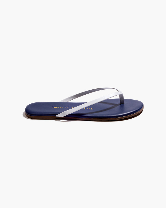 A pair of Petite Plume x TKEES Lily Sandals in navy with white straps, photographed from above on a white background. "THE PETITE PLUME" is printed in gold on the insoles.