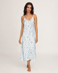 A woman stands barefoot on a plain background, facing forward with a relaxed expression, wearing the Petite Plume x White Elephant Women’s Silk Cosette Nightgown—an ankle-length white slip dress adorned with blue floral patterns.