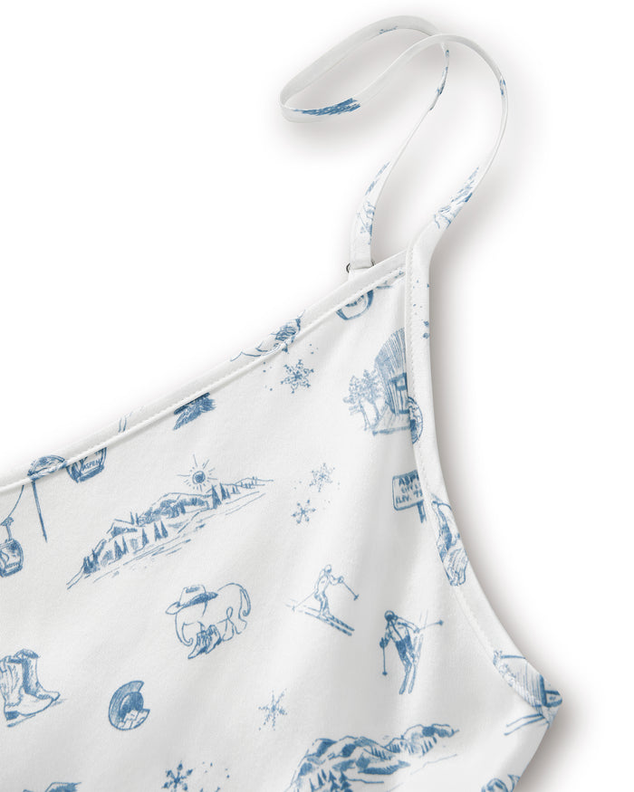 Close-up of the Petite Plume x White Elephant Women’s Silk Cosette Nightgown, featuring white fabric adorned with blue winter-themed illustrations—such as mountains, a skier, a snowflake, and a log cabin—and including a strap detail.