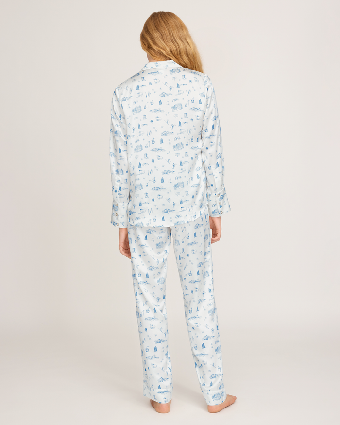 A person with long blonde hair stands barefoot facing away, wearing the Petite Plume x White Elephant Women’s Silk Pajama Set against a plain light background.