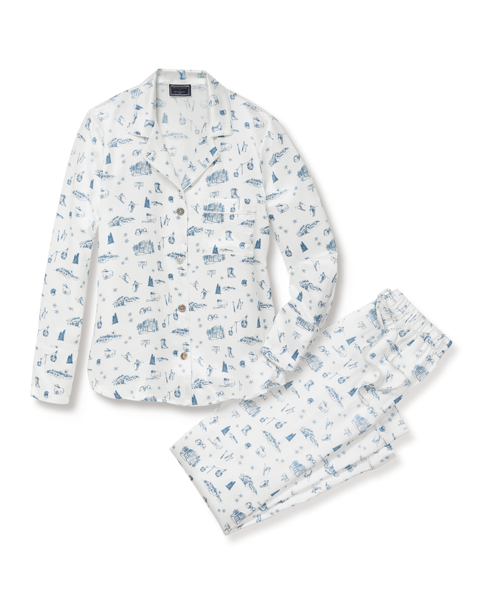 The Petite Plume x White Elephant Women’s Silk Pajama Set is shown laid flat on a white background. This set features a long-sleeve, button-up top and matching pants in white silk, adorned with blue hand-drawn illustrations.