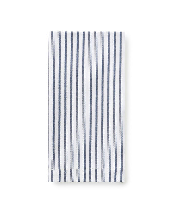 A set table with navy blue and white striped napkins, placed on a plate, with a decorative napkin ring, surrounded by cutlery and a patterned tablecloth in the background.