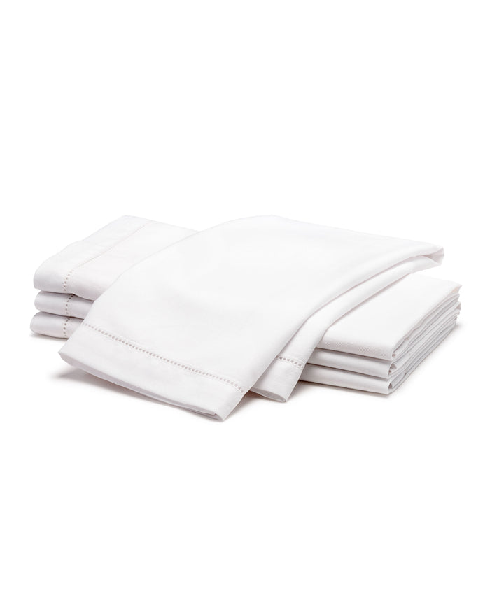 A neatly folded stack of Signature Twill Napkins in White by Petite Plume, placed on a white background. The napkins appear clean and crisp, emphasizing their soft texture and quality fabric.