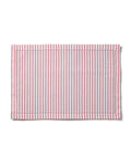 The table setting includes a white plate and red floral napkin, elevated by elegant linens and cream-handled utensils. Featuring Petite Plumes Signature Twill Placemats in Antique Red Ticking, it is adorned with white wine, meringues, a red ornament, and candle on the striped cloth.