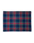 A cozy tablescape features white plates on Signature Twill Placemats in Windsor Tartan by Petite Plume, each with a matching napkin tied in a gold ring. A wine glass, fork, knife, corkscrew, candle, and vibrant bouquet of red flowers complete the look with versatile red, blue, and green hues.