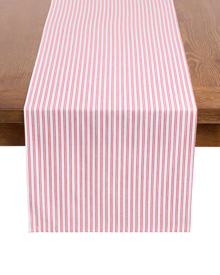 Elevate your festive tablescape with the Signature Twill Table Runner in Antique Red Ticking by Petite Plume, featuring red and white vertical stripes that complement your favorite table linens on a wooden surface.