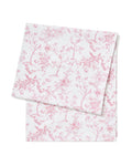 The Signature Twill Table Runner in Pink Timeless Toile, featuring a pink floral and bird pattern, is neatly folded and displayed on a white background.