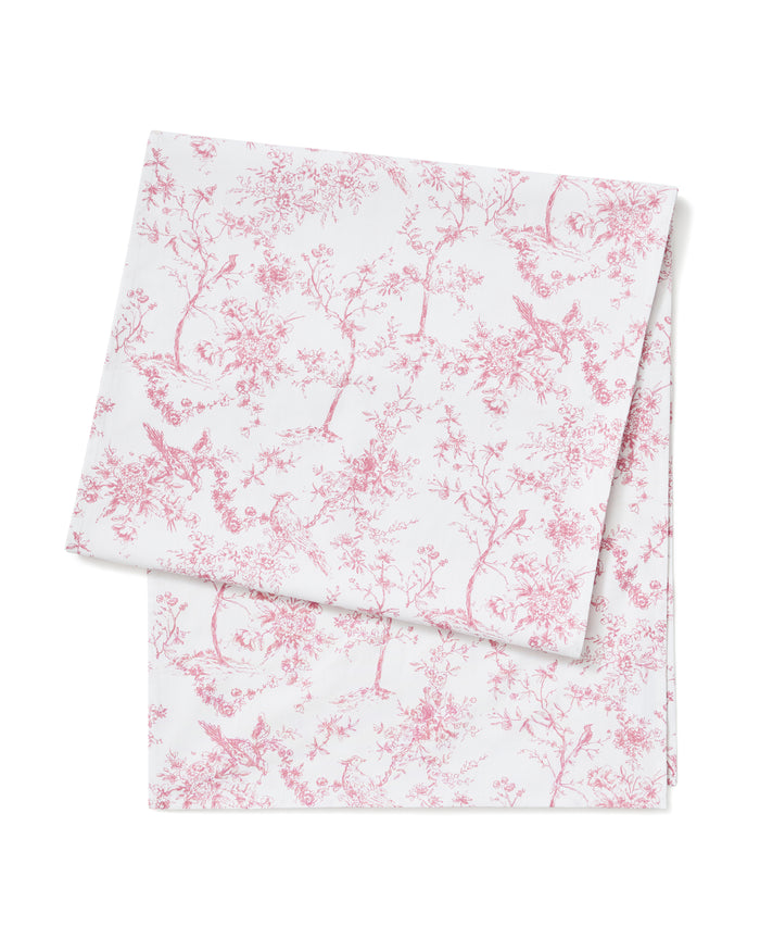 The Signature Twill Table Runner in Pink Timeless Toile, featuring a pink floral and bird pattern, is neatly folded and displayed on a white background.