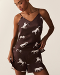 A person wears the Women’s Silk Cami Short Set in Highgrove Equestrian, featuring a dark brown base with a white horse print, standing against a plain background.