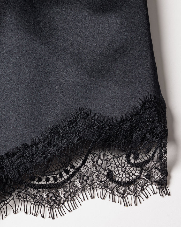 Close-up of the Womens Silk Lace Cami Short Set in Black by Petite Plume. This luxury silk sleepwear features intricate floral lace trim for elegance, a smooth satin-like finish, and is machine-washable for convenience. Contrasting textures of lace and solid fabric add visual interest.