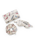 A Silk Pochette in Regatta Royale, featuring a matching sleep mask and scrunchie in white silk adorned with nautical-themed prints of anchors, ships, stars, and ropes, all arranged neatly on a white background.