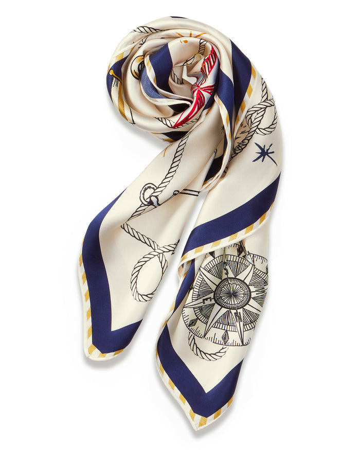 The Silk Scarf in Regatta Royale showcases nautical designs—ropes, anchors, and a compass—in blue, gold, and cream tones, all neatly arranged in a spiral pattern.