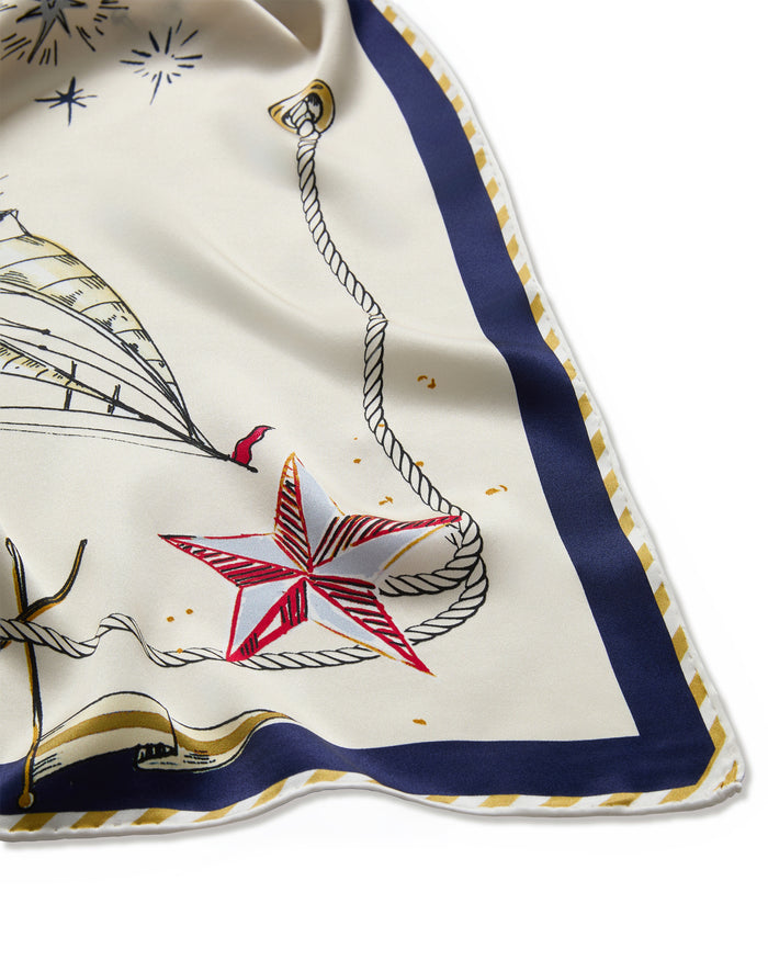 A close-up of the Silk Scarf in Regatta Royale, showcasing nautical motifs such as a red star, rope detailing, and a partial sailboat illustration on a cream background, finished with a navy and gold-trimmed border.