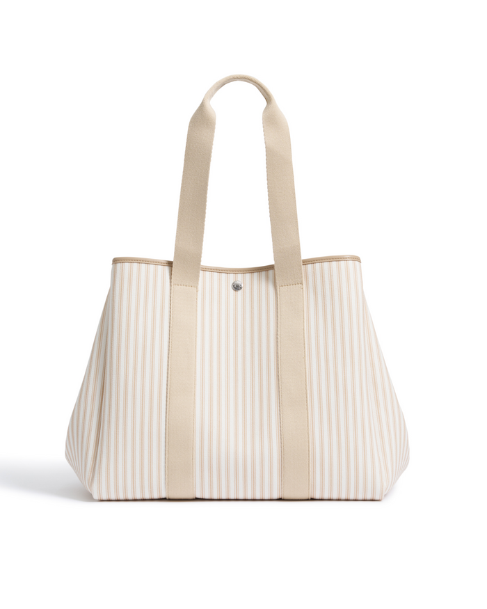 The Beckett Canvas Tote Bag in Camel Ticking features beige and white stripes, two long handles, and a snap button closure, shown standing upright on a white background.