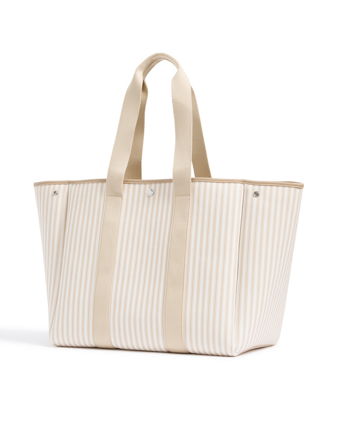 The Beckett Canvas Tote Bag in Camel Ticking features beige and white stripes, two beige handles, and vertical beige straps on the sides, displayed standing upright on a white background.