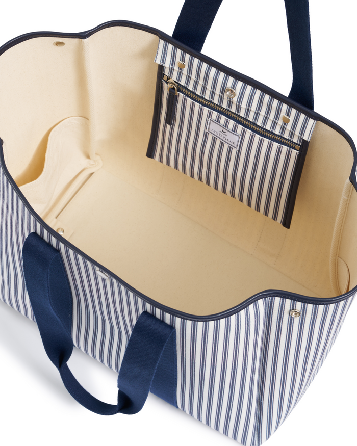 The Beckett Canvas Tote Bag in Navy French Ticking features a spacious, cream-colored interior, sturdy navy handles, and an inner zippered pocket with a matching striped design. Its open style and large size are highlighted by classic navy and cream vertical stripes.