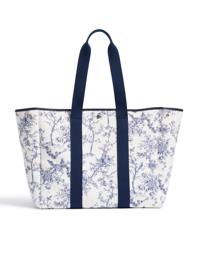 The Beckett Canvas Tote Bag in Timeless Toile, featuring a blue floral print and navy blue handles and trim, stands upright on a white background.
