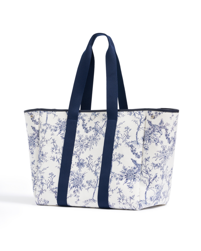 Introducing The Beckett Canvas Tote Bag in Timeless Toile: a white canvas tote adorned with a blue floral and bird print, featuring two wide navy blue handles and matching trim.