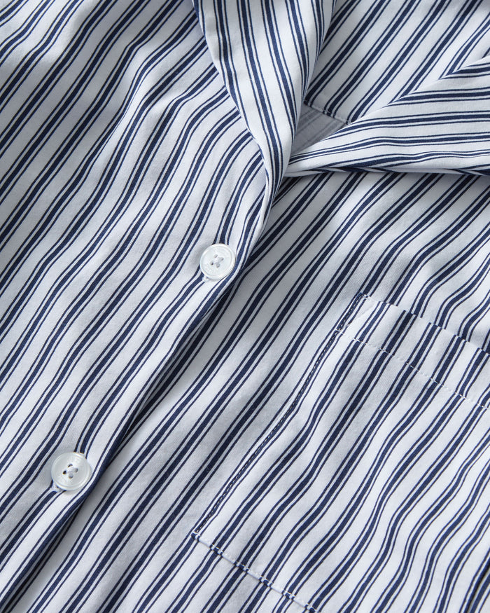 The Olivia Pima Short Set in Navy French Ticking features a matching set of blue and white vertical striped pajamas with a long-sleeve, button-up shirt with chest pocket and drawstring shorts.