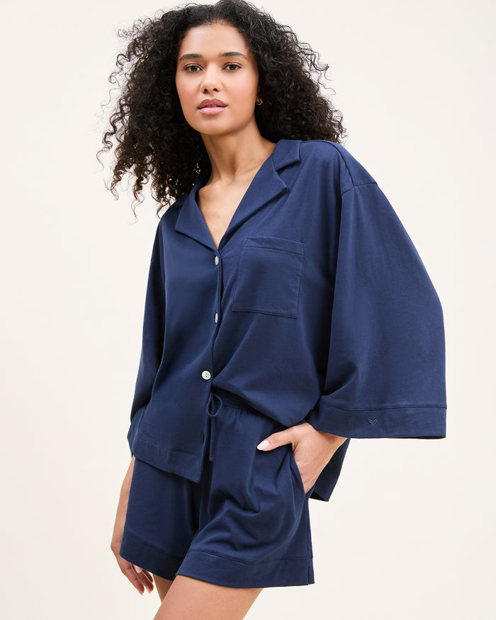 The Olivia Pima Short Set in Navy features a short-sleeve button-up top with a chest pocket and matching drawstring shorts, both displayed flat on a white background.