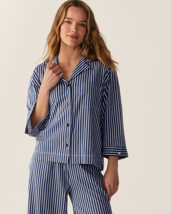 A woman wearing The Olivia Wide Leg Pima Pajama Set in Admiral Ticking, featuring a navy and white striped button-front shirt with 3/4 sleeves, a notched collar, and matching wide-leg pants.
