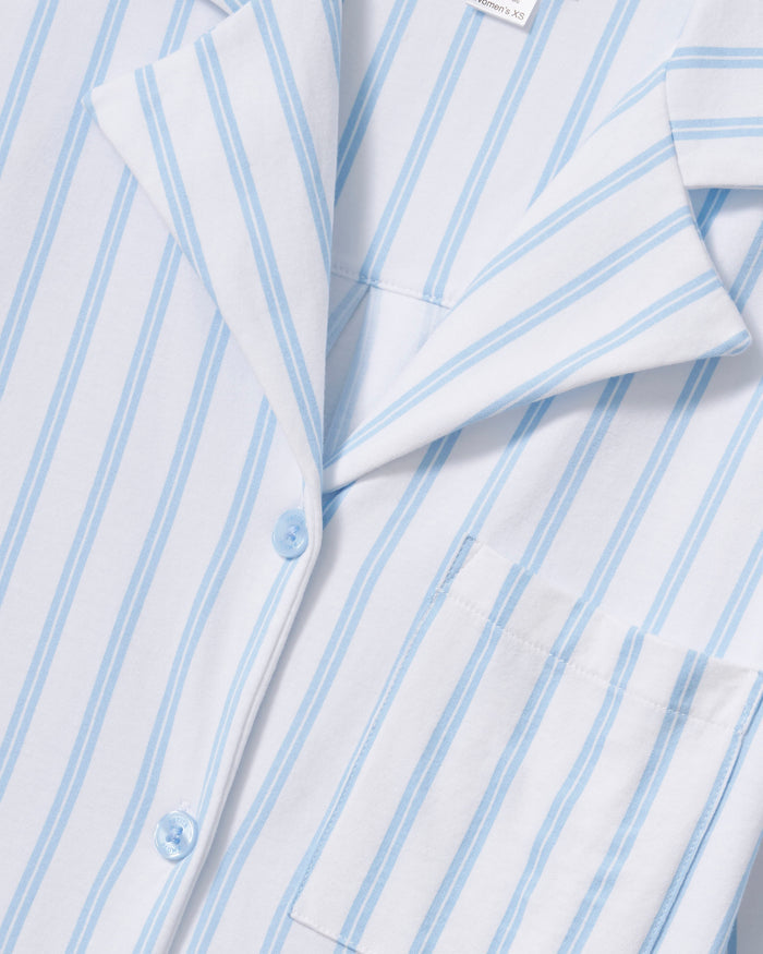 A person models the Petite Plumes Olivia Wide Leg Pima Pajama Set in Periwinkle Stripe, featuring a soft, luxurious white and light blue striped button-up long-sleeve shirt with matching wide-leg pants against a plain background that enhances its elegant simplicity.