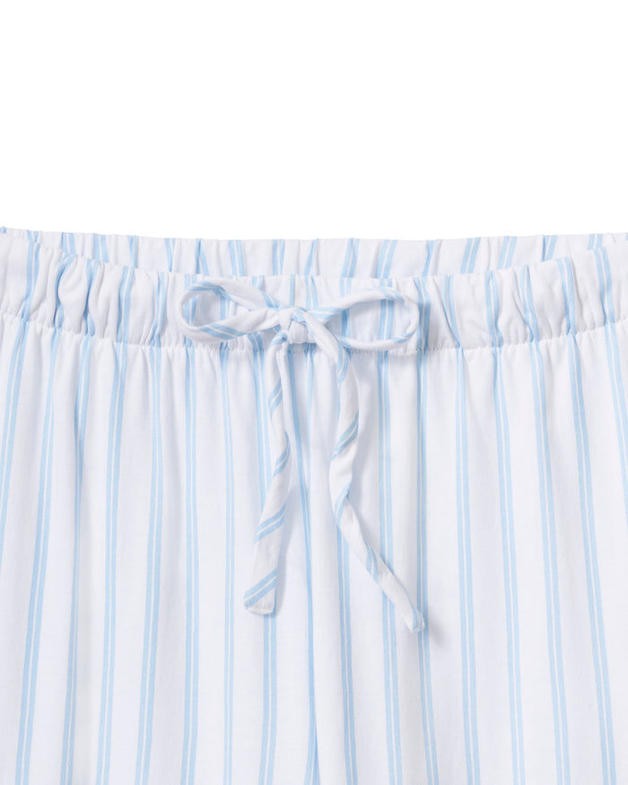 A person models the Petite Plumes Olivia Wide Leg Pima Pajama Set in Periwinkle Stripe, featuring a soft, luxurious white and light blue striped button-up long-sleeve shirt with matching wide-leg pants against a plain background that enhances its elegant simplicity.