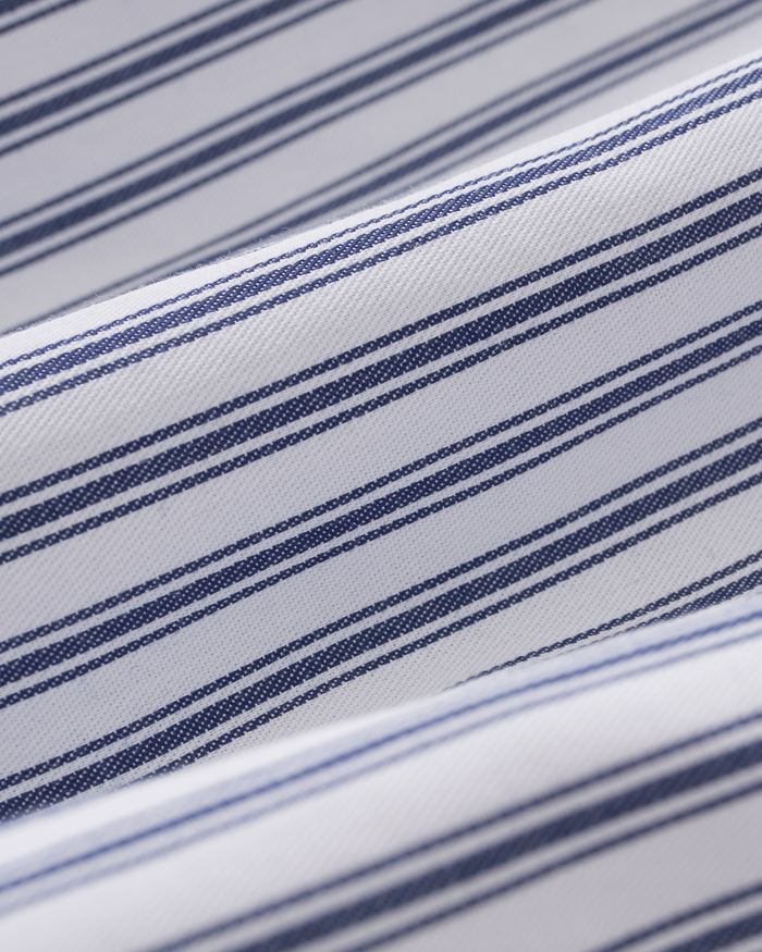 Close-up of The Celine Poplin Pajama Set in Navy French Ticking, featuring white fabric adorned with navy blue horizontal stripes of varying thicknesses in a repeating pattern. The pajama set fabric is shown folded or draped, highlighting its soft curves and texture.