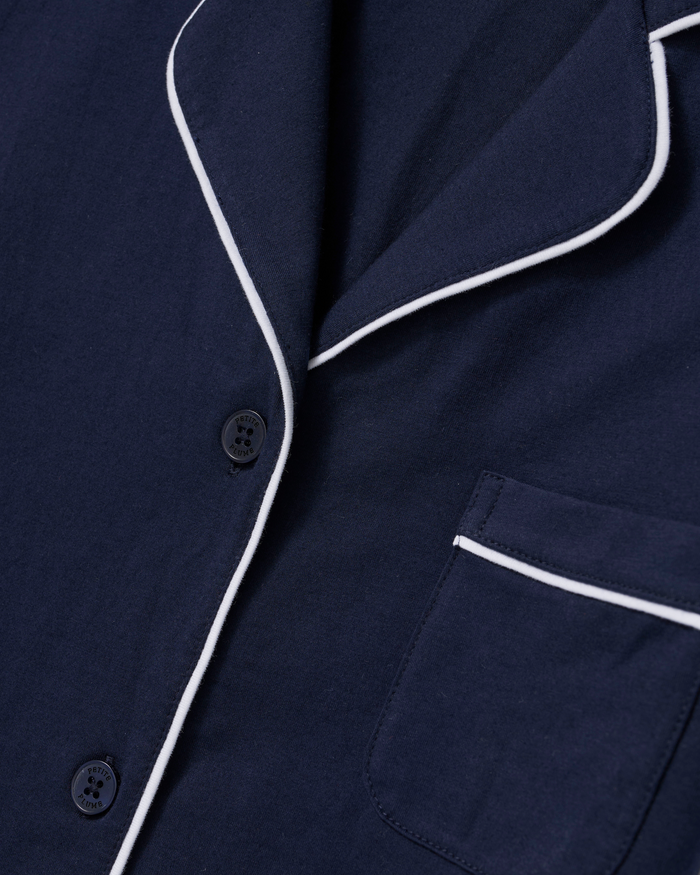 Close-up of The Poppy Lightweight Pima Short Set in Navy, featuring a navy blue pajama top with white piping along the collar, button line, and pocket. Two black buttons and a pocket with white trim are visible.