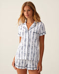 A woman wearing The Poppy Pima Short Set in Navy Mayfair Toile, featuring a matching short-sleeve top and shorts with a blue and white floral pattern, stands against a light background.