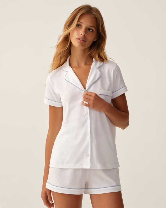 Wearing the Greek Embroidered Poppy Pima Short Set in white with periwinkle piping, a person stands against a plain light background.