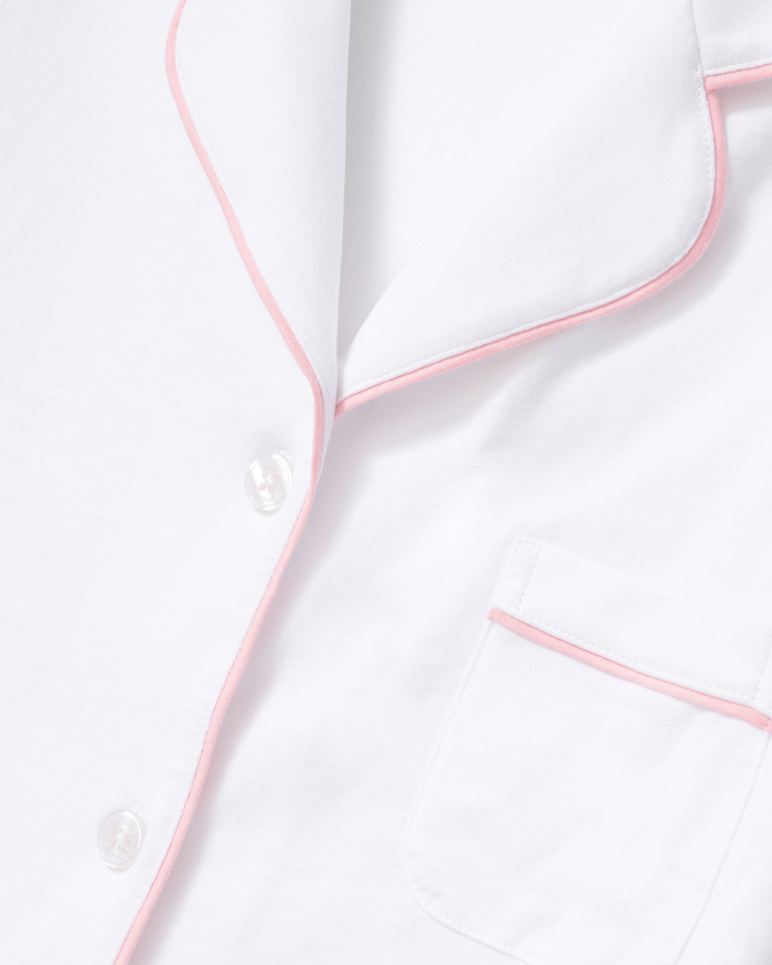 Here’s a rewritten sentence using your product data: A close-up of The Poppy Pima Short Set in White with Pink Piping showcases its soft, smooth fabric, pink piping accenting the collar, chest pocket, and button placket, as well as white buttons and a chest pocket.