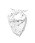 A fluffy white dog with small ears wears the Petite Plume Par Avion Dog Bandana featuring a blue floral pattern. The happy pup lies on a light wooden floor, looking up with its mouth open, showcasing the perfect blend of style and comfort in dog accessories.