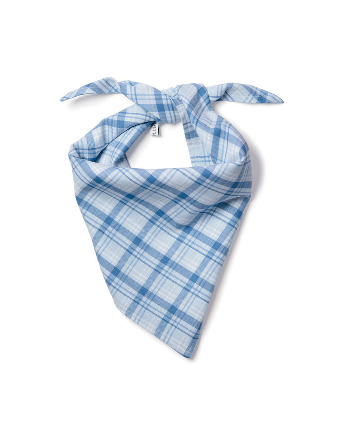 A fluffy white dog with pointy ears sits on a wooden floor, donning a charming Dog Twill Bandana in Seafarer Tartan from Petite Plume. With an open mouth and cheerful expression, the pup looks directly at the camera, adding warmth to the scene.
