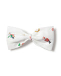 The Petite Plume A Night at the Nutcracker Dog Bow Tie is white and adorned with festive illustrations like Santa Claus, Christmas trees, candy canes, and snowflakes, creating a cheerful holiday accessory for your furry friend.