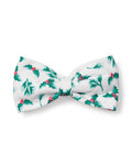 The Petite Plume Dog Bow Tie in Sprigs of the Season features a festive white fabric adorned with green holly leaves and red berries, perfect for holiday pet fashion.