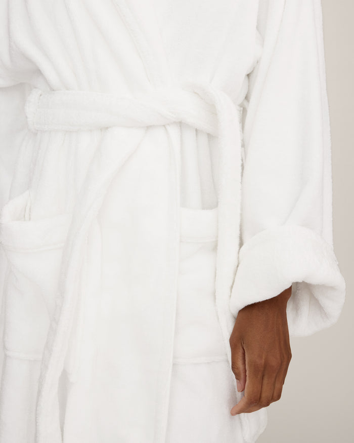 The Unisex Luxe Terry Robe in White features long sleeves, a shawl collar, two front pockets, and a waist tie belt, displayed against a white background.