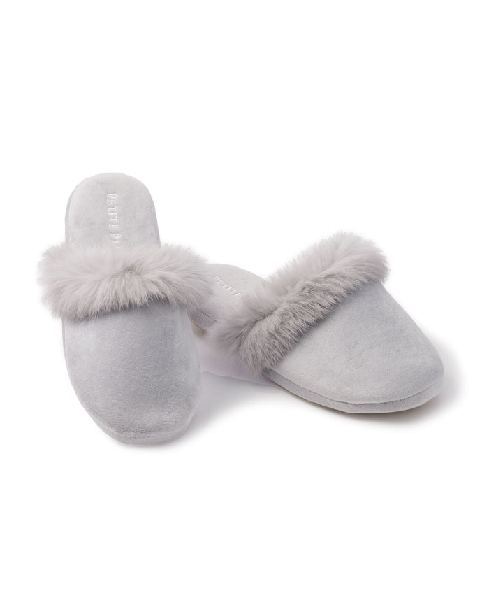 A pair of Womens Faux Fur Trim Slippers in light gray by Petite Plume, showcasing plush comfort with soft fur trim, is displayed on a white background. One slipper stands upright while the other rests elegantly on its side.