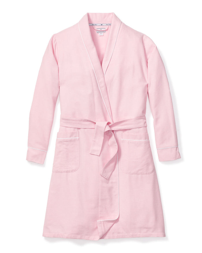 The Womens Flannel Robe in Pink by Petite Plume is a luxurious light pink bathrobe with long sleeves, two front pockets, a matching belt for the waist, and elegant white piping. Its crafted from high-quality cotton and laid flat against a white background for indulgent lounging.