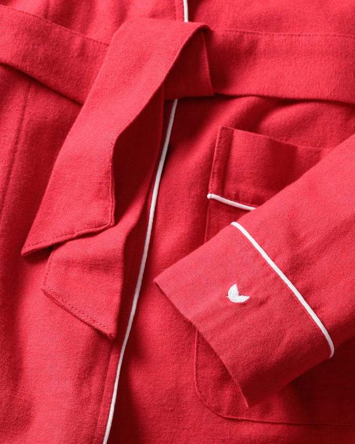 Close-up of Petite Plume’s Womens Flannel Robe in Red with White Piping, highlighting a folded belt, pocket, and sleeve cuff. The cuff has a small white embroidered crescent detail, enhancing the robes luxurious charm.