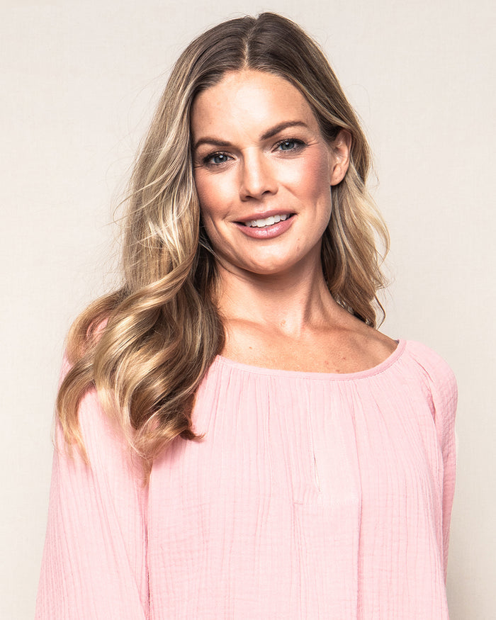 A woman with long, wavy blonde hair wears a light pink Womens Gauze Willow Scoopneck Top by Petite Plume and smiles at the camera against a plain background.