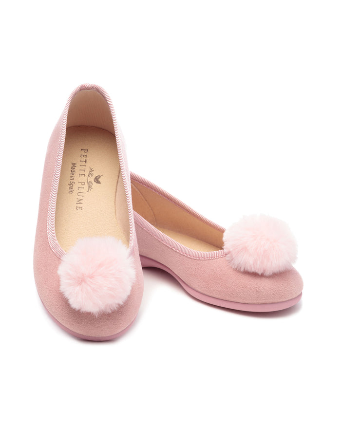 The Womens Juliette Slipper by Petite Plume in Antique Rose Suede features a festive pom-pom on the toes. This luxury footwear boasts a smooth texture and labeled insoles, promising comfort with every step on a white background.