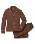A woman stands barefoot in the Women's Lightweight Pima Pajama Set in Chocolate Brown, featuring a button-up long-sleeve shirt with white piping and matching pants, against a plain white background.
