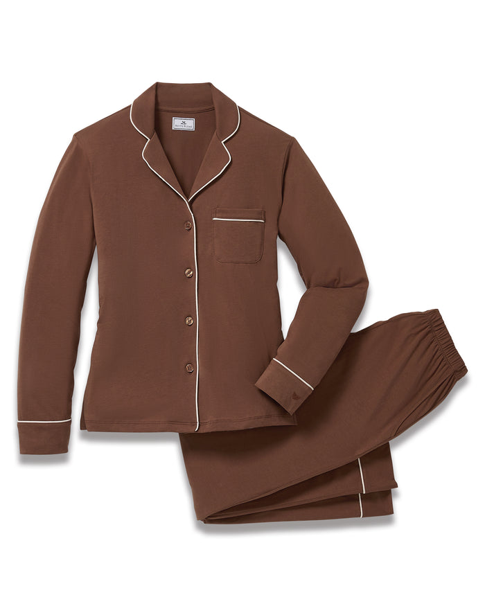 A woman stands barefoot in the Women's Lightweight Pima Pajama Set in Chocolate Brown, featuring a button-up long-sleeve shirt with white piping and matching pants, against a plain white background.