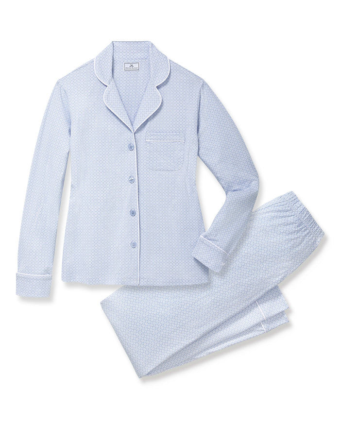 A woman with light brown hair and a neutral expression stands barefoot against a plain background, modeling the Women's Lightweight Pima Pajama Set in Periwinkle Geo—featuring long sleeves, button-up top with collar, and matching pants.