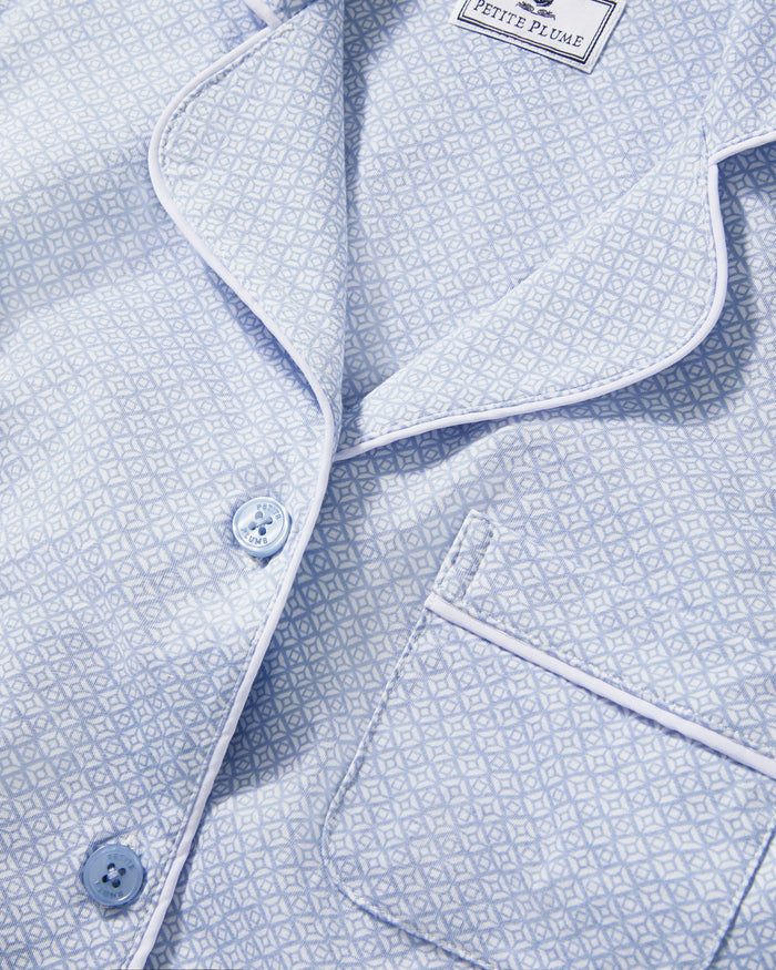 A woman with light brown hair and a neutral expression stands barefoot against a plain background, modeling the Women's Lightweight Pima Pajama Set in Periwinkle Geo—featuring long sleeves, button-up top with collar, and matching pants.