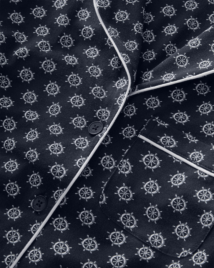 Close-up of the Women’s Lightweight Pima Short Sleeve Short Set in Captain’s Compass, featuring dark fabric with a white nautical ship wheel pattern, white piping along the edges, buttons, and a visible chest pocket.