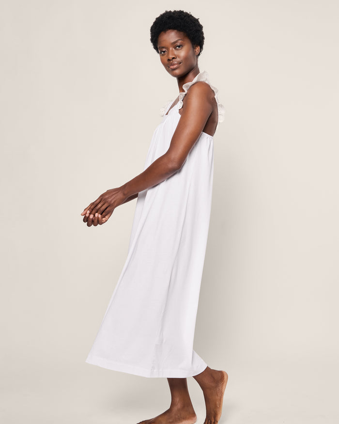 A person with short curly hair stands barefoot on a neutral background in a Petite Plume Womens Pima Clara Nightgown in white, evoking the grace of a serene bedtime ritual with one arm slightly forward.