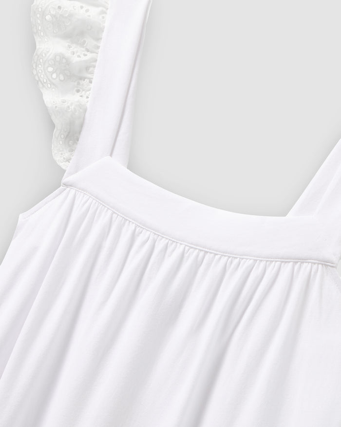 A close-up of the Womens Pima Clara Nightgown in white by Petite Plume shows its gathered fabric and wide shoulder straps. Made from breathable material, it features lace details on the straps for an elegant touch against a plain, light gray background, exuding luxurious sleepwear charm.