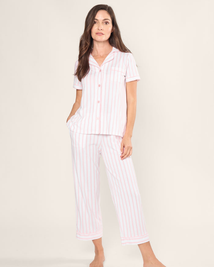 A person stands barefoot in the Womens Pima Crop Set by Petite Plume, featuring a vintage-inspired short-sleeved, button-up top with a collar and cropped pants. Made from soft Peruvian Pima cotton, it displays pink and white stripes against a plain white background.